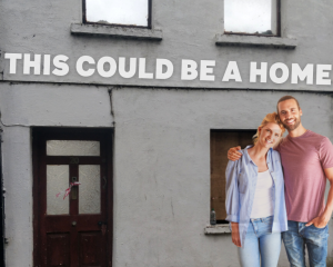 Young couple standing outside a vacant house with the line 'This could be a home'