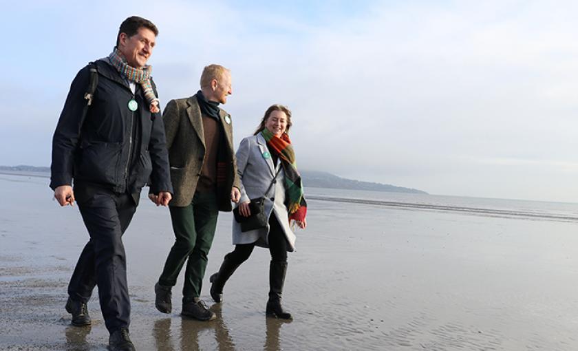 A photo of three people walking along a beach.