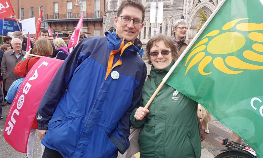 Green Party Leader Eamon Ryan and Green Party volunteer Mary Ryder wave a flag at a protest.
