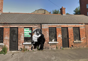 On a boarded up house there is an image of a mother and her child with the slogan, "This could be a home".