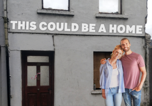 Young couple standing outside a vacant house with the line 'This could be a home'