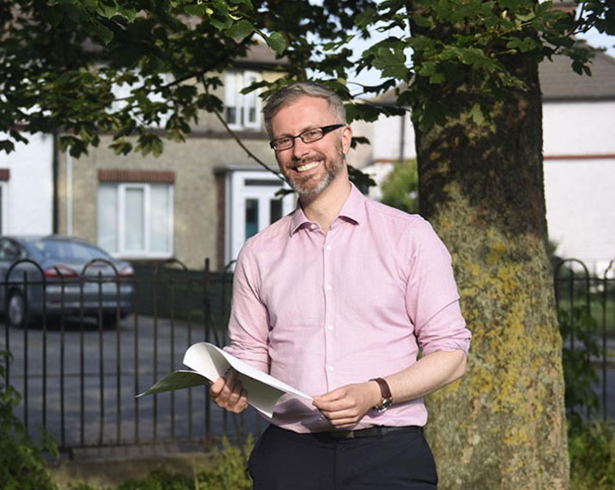 Minister Roderic O'Gorman holding the Gender Pay Gap Information Bill July 2021, standing by a tree with houses in the background
